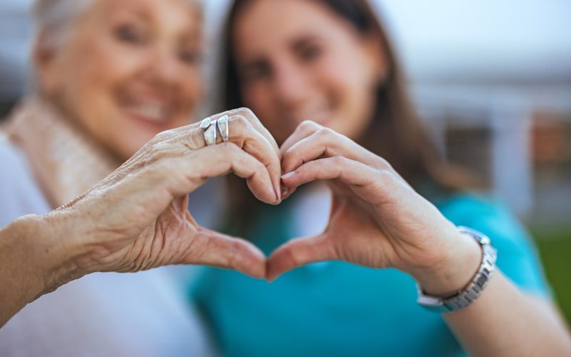 Elderly Woman and Caregiver Forming Heart Shape with Hands