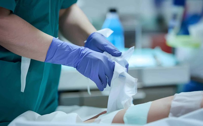 A nurse in gloves carefully changes the dressing on a patient's wound in a medical facility, showcasing attentive healthcare practices.